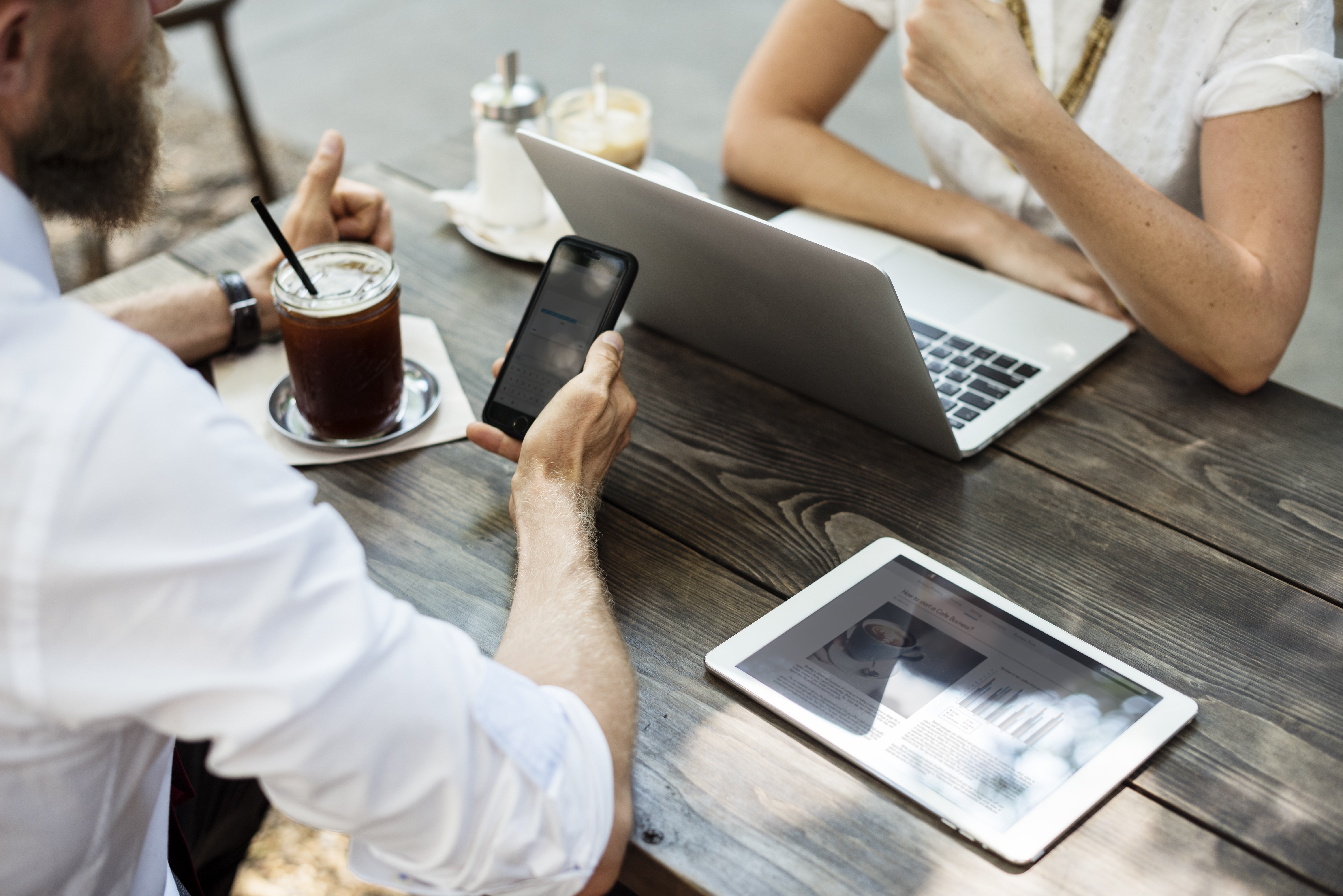 To personer ved et cafébord med telefon, bærbar computer og tablet