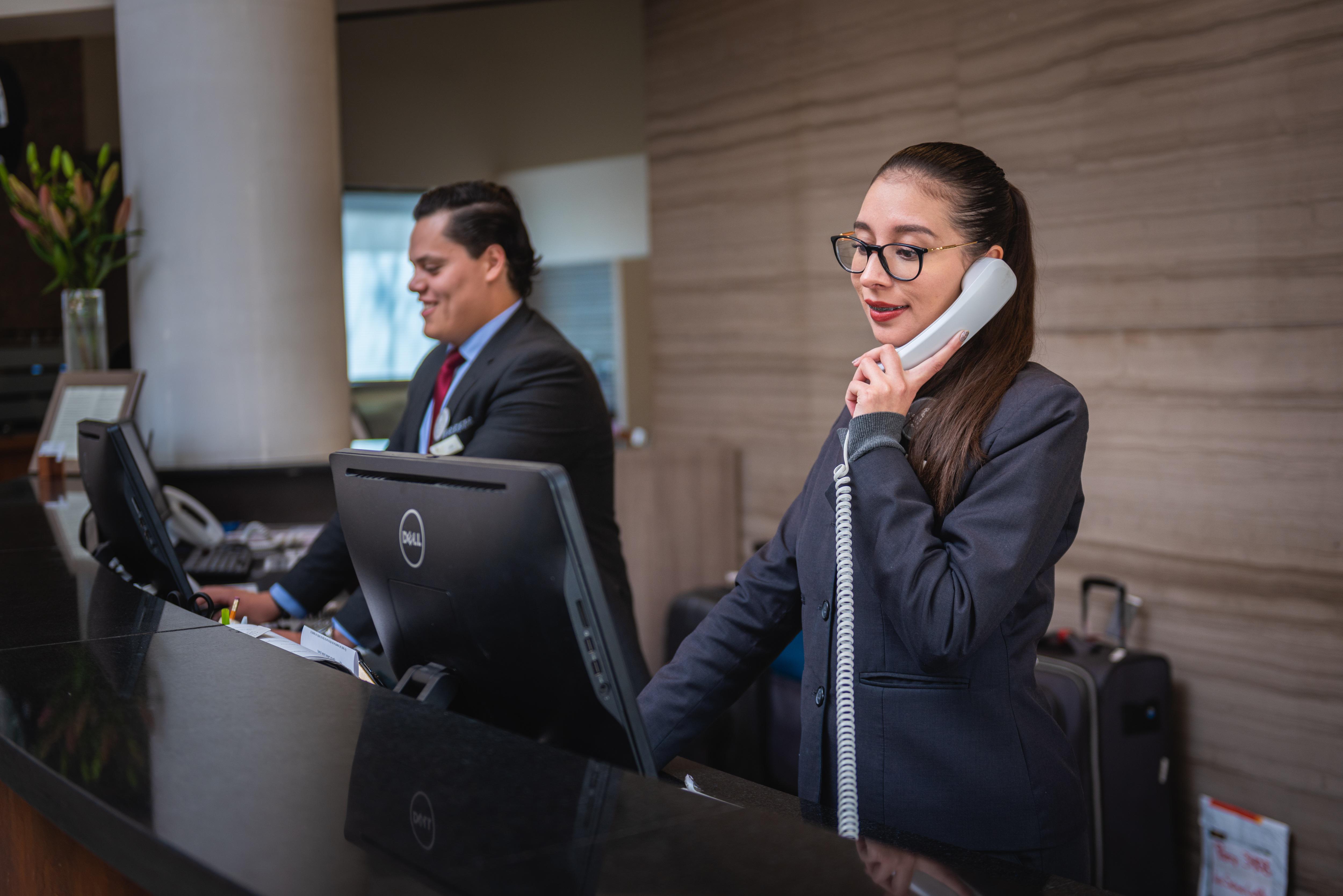 Hotellets receptionsmedarbejdere hjælper gæster ved skranken og i telefonen